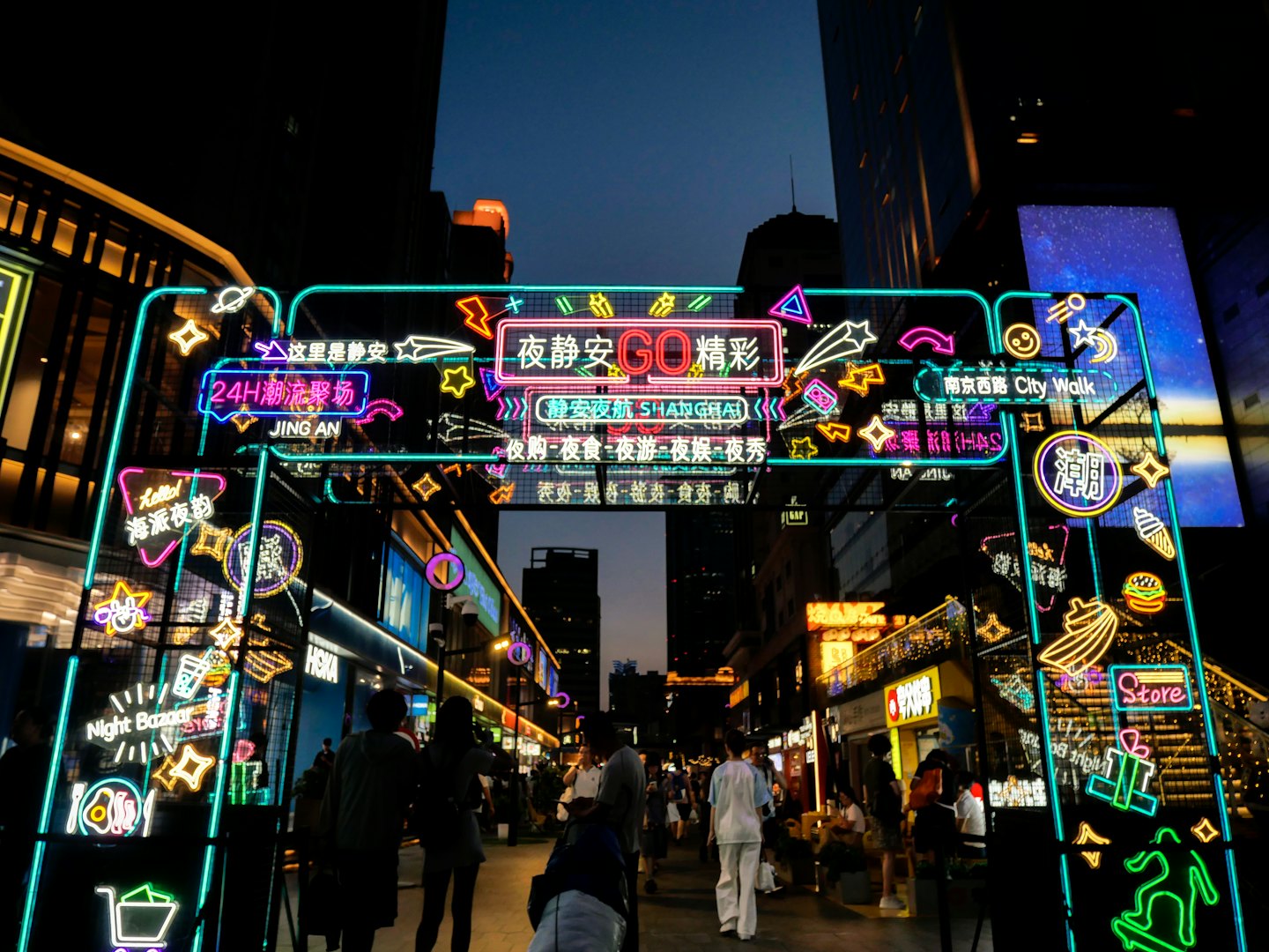 Pedestrians walk under bright neon signs in a busy city.